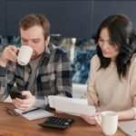 A couple reviewing bills, using a calculator and smartphone, in a modern kitchen.